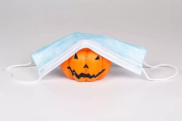 Concept Halloween , COVID-19 prevention. Pumpkin candle with medical mask