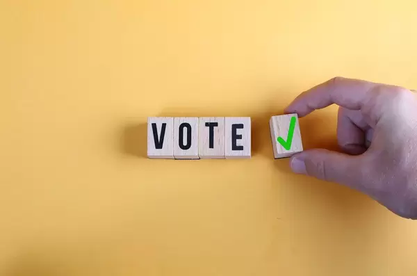 Concept of voting yes or positive vote. Male hand placing wooden cube with check mark yes symbol next to the cubes with the word vote