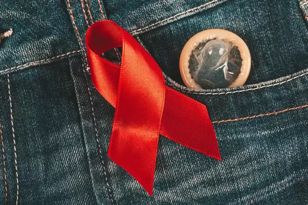 Condom peeking out from jeans pocket with red awareness ribbon for aids and hiv