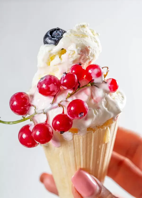 Cone with vanilla ice cream and fresh red currant berries in a woman's hand (Flip 2019)