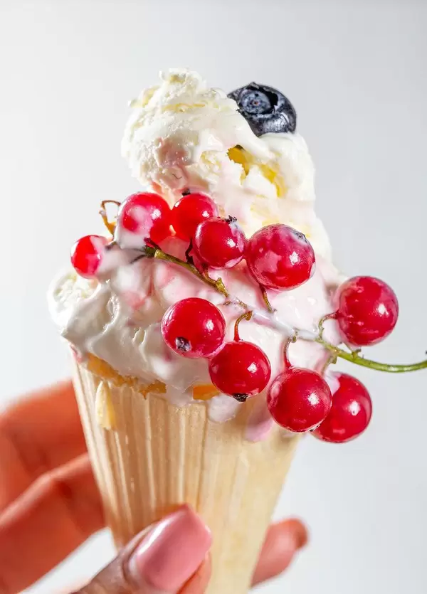 Cone with vanilla ice cream and fresh red currant berries in a woman's hand