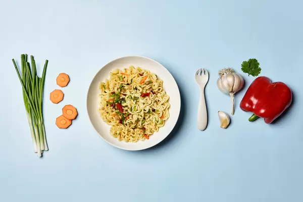 Cooked quick instant noodles with food ingredients on bright blue background