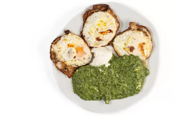 Cooked Spinach and Fried Eggs isolated above white background