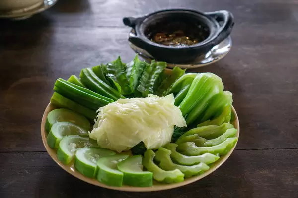 Cooked Zucchini, Cabbage, Bitter Melon, Okra and Winged Bean on a Plate with Pork Stew in a Clay Pot