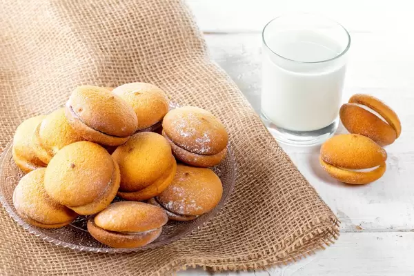 Cookies with cream and coconut on a wooden table with a glass of milk