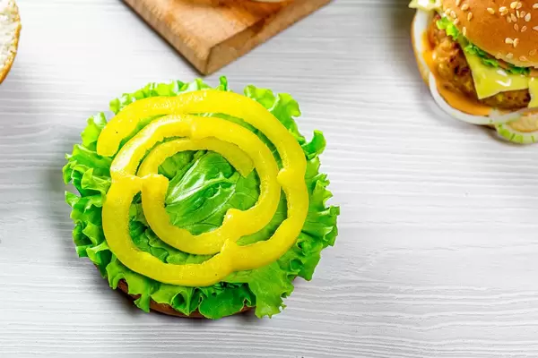 Cooking vegan burgers with fresh lettuce leaves and pieces of yellow pepper