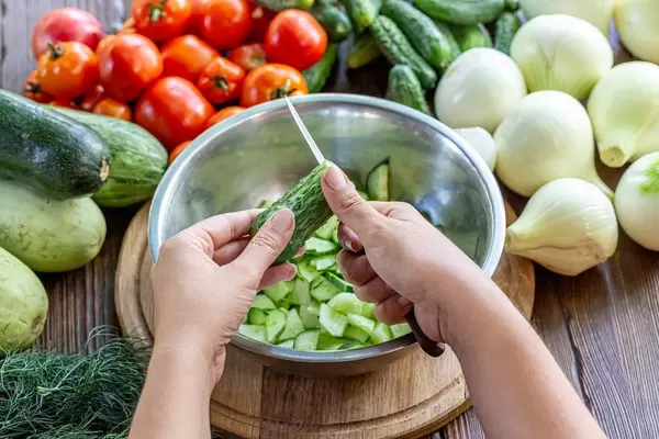 Cooking vegetable salad with fresh vegetables. Women's hands cut cucumber