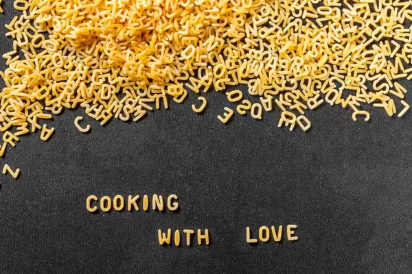 Cooking with Love aus Buchstaben-Pasta auf schwarzem Hintergrund