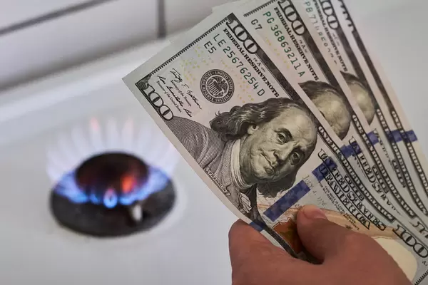 Cooktop with burning gas ring and hand of person holding pile of us dollars