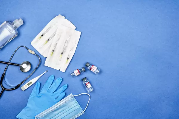 Corona-Impfstoff und Zubehör wie Spritzen und Maske vor blauem Hintergrund mit Platz für Text
