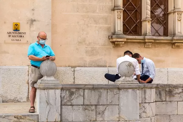 Corona-Maßnahmen in Spanien: drei Männer mit Mundschutz vor dem Rathaus von Alcudía (Mallorca)
