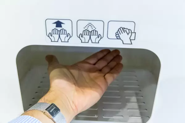 Corona und Reisen: die Hand eines Reisenden am Flughafen BER wird kontaktlos desinfiziert