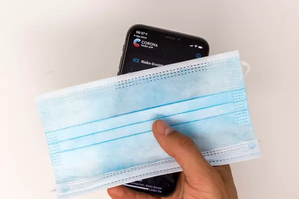 Coronavirus Infektionsschutz: Smartphone mit Corona-Warn-App und OP-Maske in der Hand