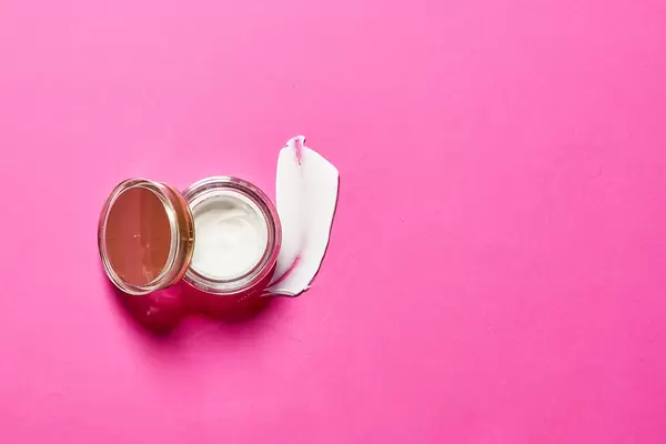 Cosmetic cream lotion opened container on bright pink background