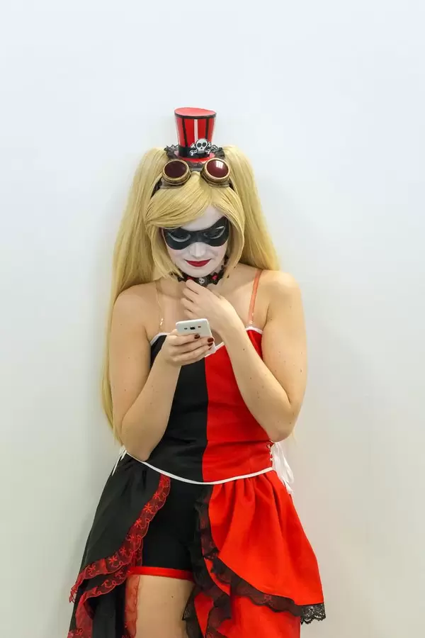 Cosplayerin mit rot-schwarzem Kleid und Schminke schaut auf ihr Handy