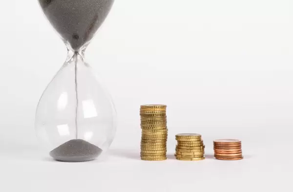 Countdown und Geld – kürzlich gestartete Sanduhr neben drei Stapeln von Münzen