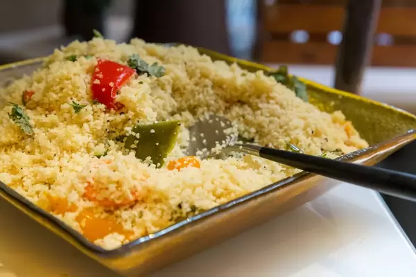 Couscous and colourful pepper salad in green bowl with spoon