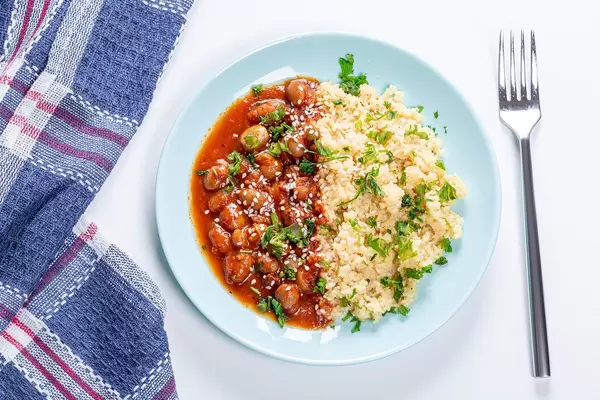 Couscous porridge with beans in tomato sauce, parsley and sesame seeds. Top view