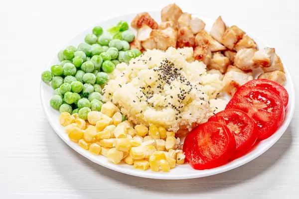 Couscous with Chia seeds, young peas, corn, tomatoes and baked chicken on a white plate (Flip 2019)