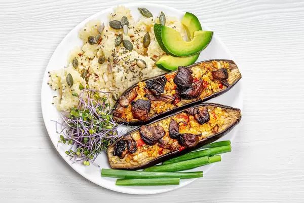 Couscous with seeds, micro greens cabbage, baked eggplant and pieces of fresh avocado and young onions on a plate