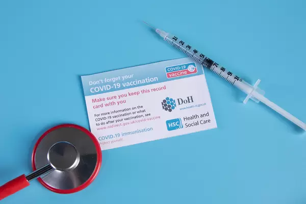 Covid-19 vaccination record card with stethoscope and syringe on blue background