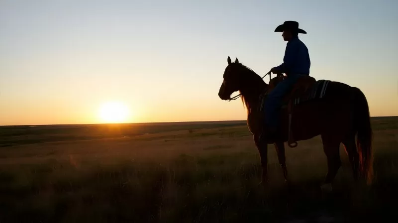 Cowboy auf Pferd reitet über weite Prärie bei Sonnenuntergang
