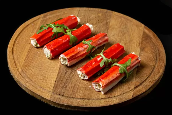 Crab sticks stuffed with cheese and herbs on a wooden round board