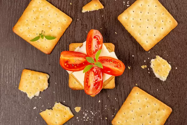 Crackers with cheese, tomato and basil leaves on a brown background