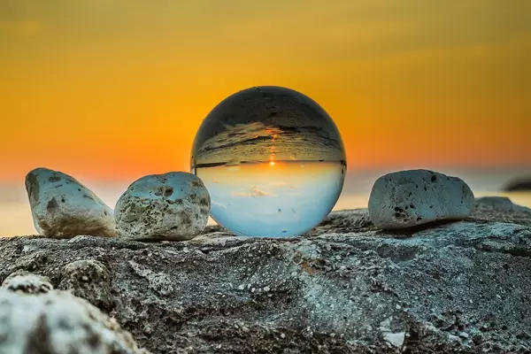 Creative Sunset Photo with flipped Sea Horizon in Lens Ball next to Stones at Golden Hour