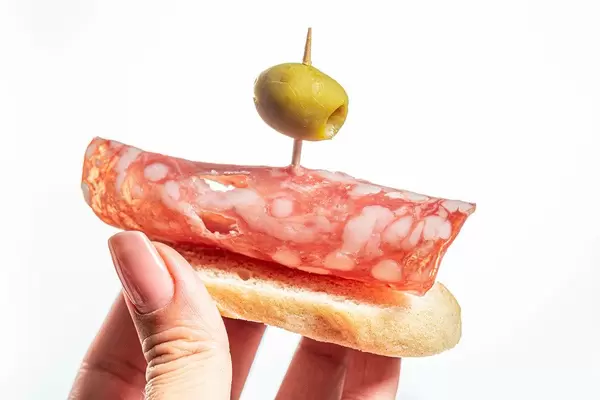 Crostini mit Salami und Olive in der Hand einer Frau vor weißem Hintergrund