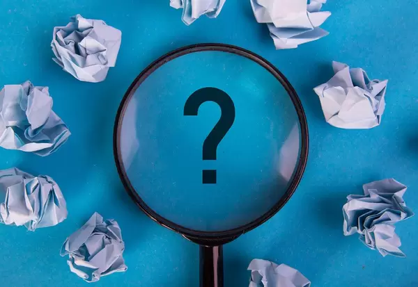 Crumpled paper balls with magnifying glass over question mark