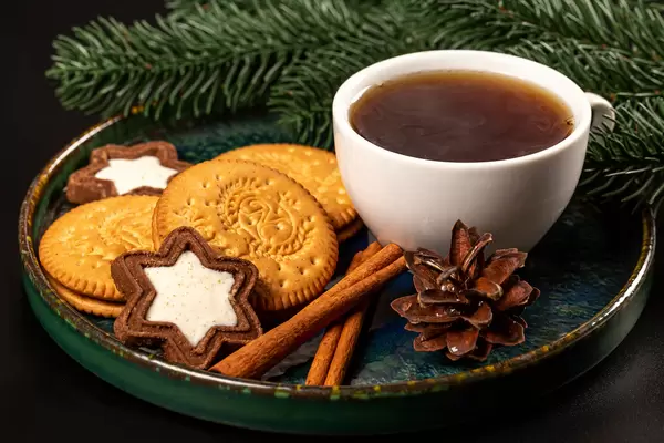 Cup of coffee with cinnamon and cookies on a dark background with branches of a christmas tree
