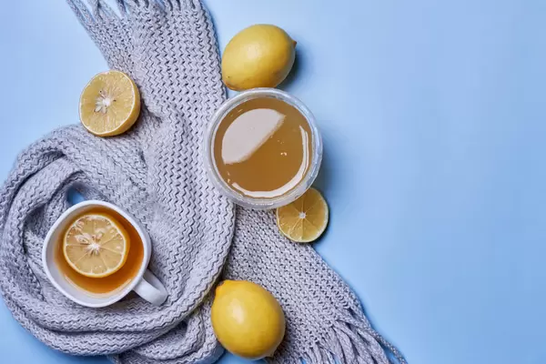 Cup of hot tea with lemon, honey and scarf on blue background