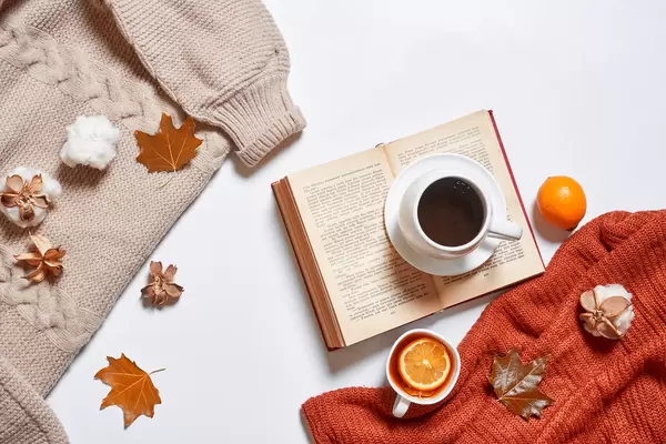 Cups of tea and coffee, cozy knitted sweaters, autumn leaves, open book on white background