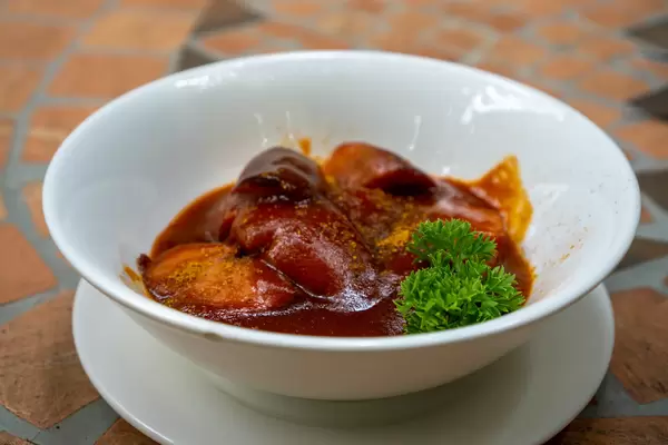 Currywurst in einer Keramikschüssel mit geschnittener Bratwurst, selbsgemachter Tomatensauce, Currypulver und Petersilie Nahaufnahme