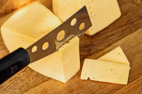 Cut cheese with cheese knife on wooden background