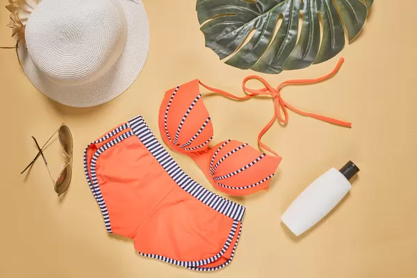 Cute female's bikini, sunglasses, straw hat and sunscreen cream on colored background