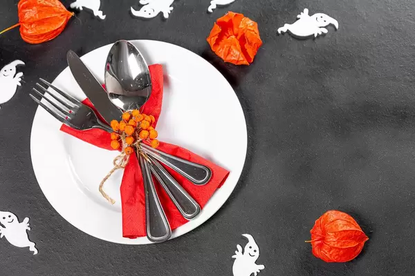 Cutlery on a black background with white ghosts and fruits of physalis. Table setting for Halloween (Flip 2019)