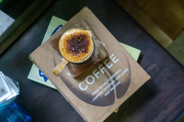 Dalgona Kaffee in einer Kaffeetasse mit Holzhenkel auf Büchern über Kaffee in einem Cafe Draufsicht