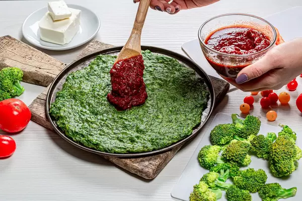 Damenhand gießt Tomatensauce mit einem Kochlöffel auf den Pizzateig