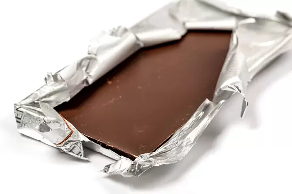 Dark chocolate bar with foil on white background