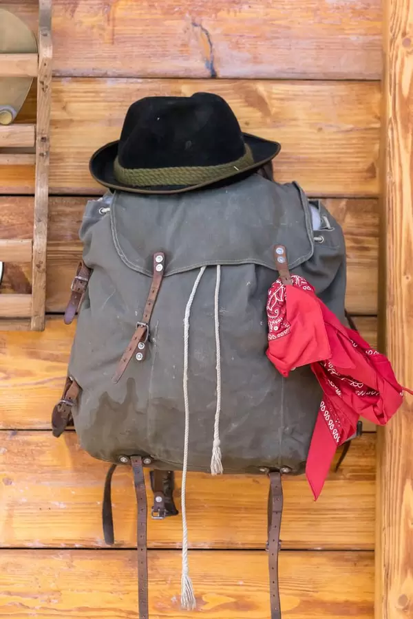Das Gepäck eines Bergwanderes mit Hut und rotem Tuch an Holzwand