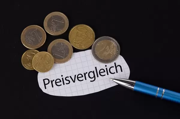 Das Konzept vom Preisvergleich: Preisvergleich Text auf einem Blatt Papier mit einigen Münzen und einem blauen Stift im schwarzen Hintergrund