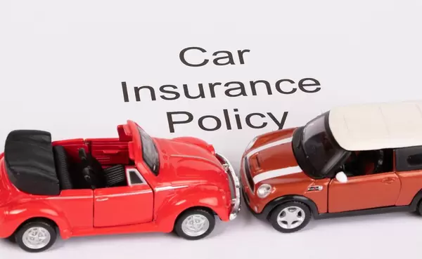 Das Konzept von Autoversicherung: Text "Car Insurance Policy" auf weißem Hintergrund mit zwei roten Spielzeugautos an einem Unfall beteiligt