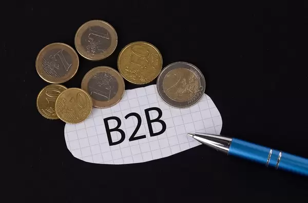 Das Konzept von B2B: B2B Text auf einem Blatt Papier mit einigen Münzen und einem blauen Stift im schwarzen Hintergrund