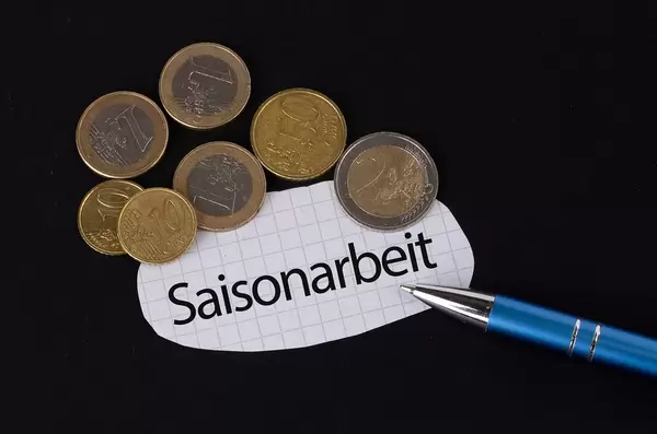 Das Konzept von der Saisonarbeit: Saisonarbeit Text auf einem Blatt Papier mit einigen Münzen und einem blauen Stift im schwarzen Hintergrund