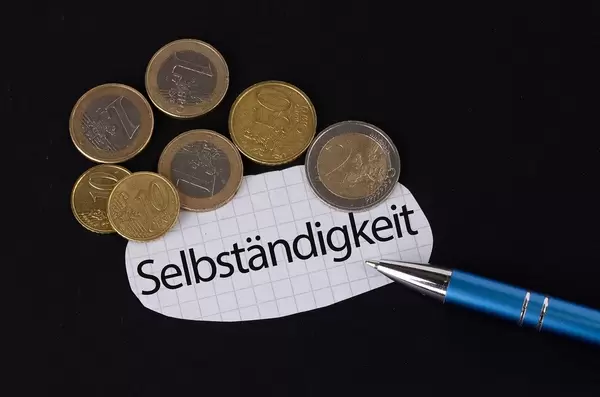 Das Konzept von der Selbständigkeit: Selbständigkeit Text auf einem Blatt Papier mit einigen Münzen und einem blauen Stift im schwarzen Hintergrund