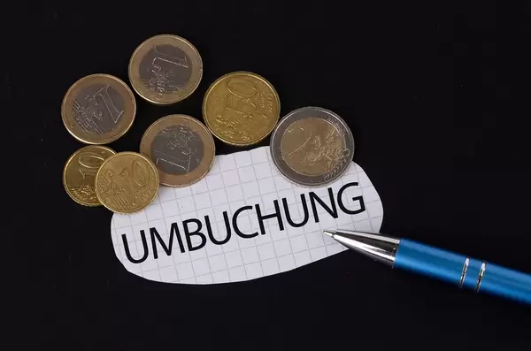 Das Konzept von der Umbuchung: Umbuchung Text auf einem Blatt Papier mit einigen Münzen und einem blauen Stift im schwarzen Hintergrund