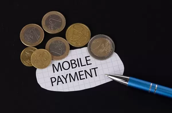 Das Konzept von Mobile Payment: Mobile Payment Text auf einem Blatt Papier mit einigen Münzen und einem blauen Stift im schwarzen Hintergrund