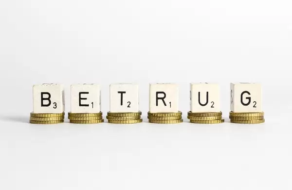 Das Wort Betrug aus Würfelbuchstaben auf Stapel aus Münzen